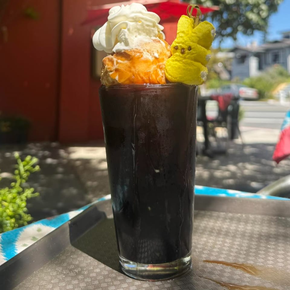 Thai iced tea with whipped cream, orange ice cream, and a yellow Peep on a tray outdoors.