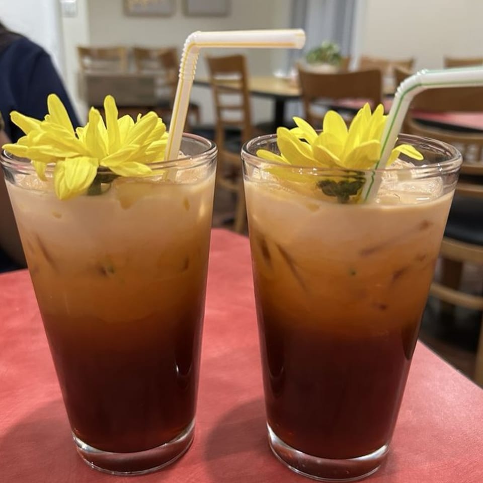 Two Thai iced teas with yellow flowers and straws on a red table in a restaurant.