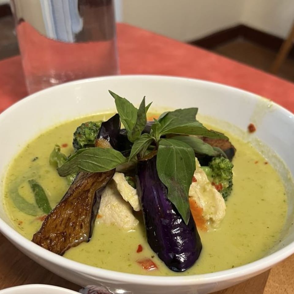 Delicious Thai Kitchen's green curry with eggplant, broccoli, chicken, and basil in a white bowl.