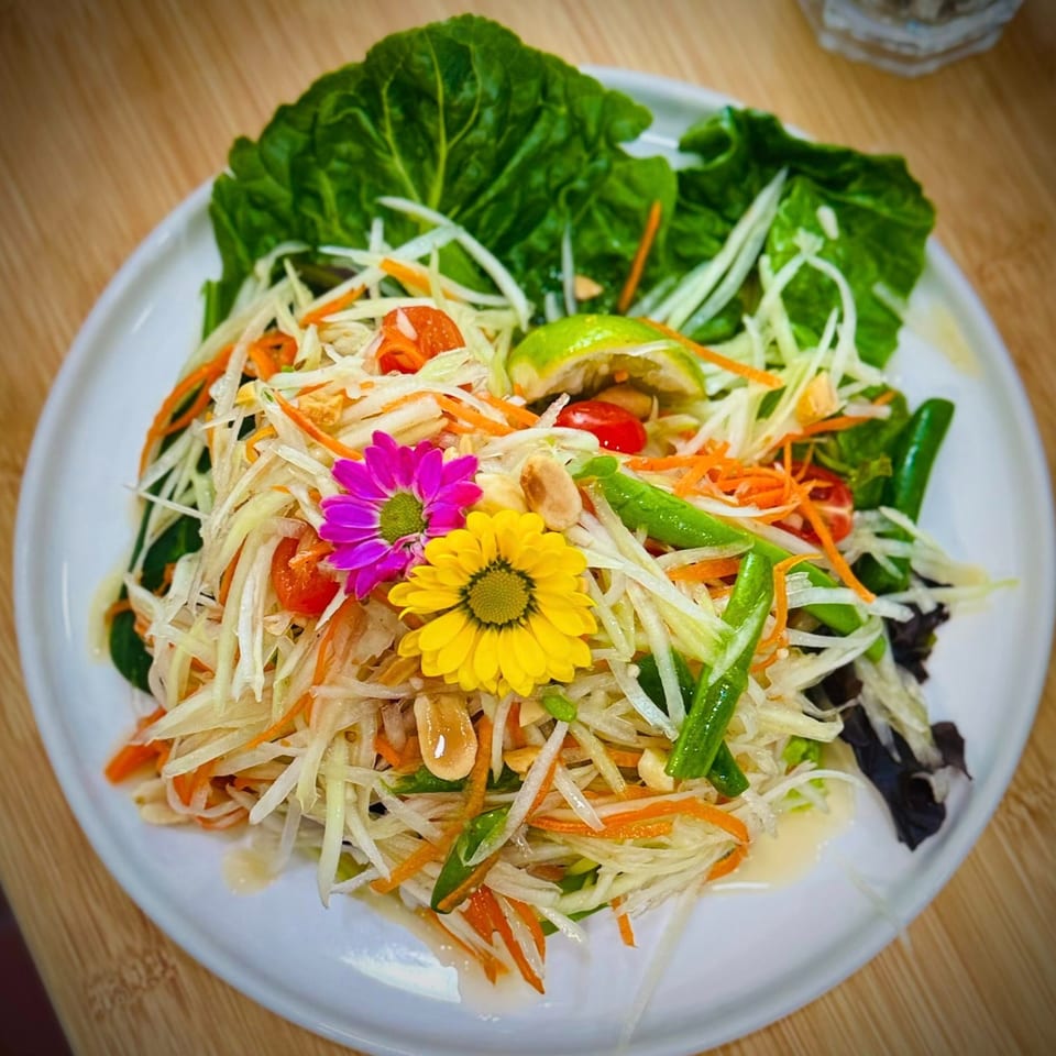Delicious Thai Kitchen's Som Tum (papaya salad) with colorful flowers, lime, peanuts, and green beans.