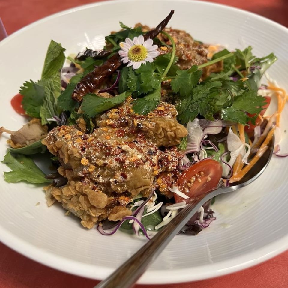 Crispy fried chicken salad with herbs, chili, and a daisy garnish in a white bowl.
