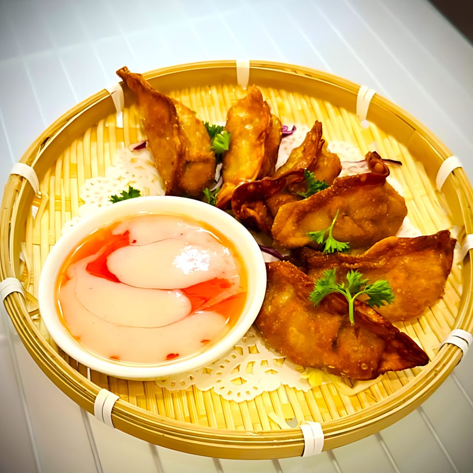 Golden fried wontons with parsley garnish and a sweet dipping sauce in a bamboo serving tray.